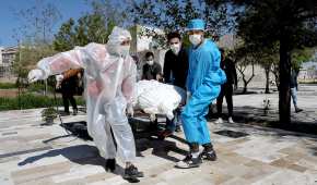 Un grupo de personas, que usan ropa protectora, llevan el cuerpo de una víctima que murió de coronavirus