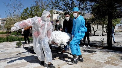 Un grupo de personas, que usan ropa protectora, llevan el cuerpo de una víctima que murió de coronavirus